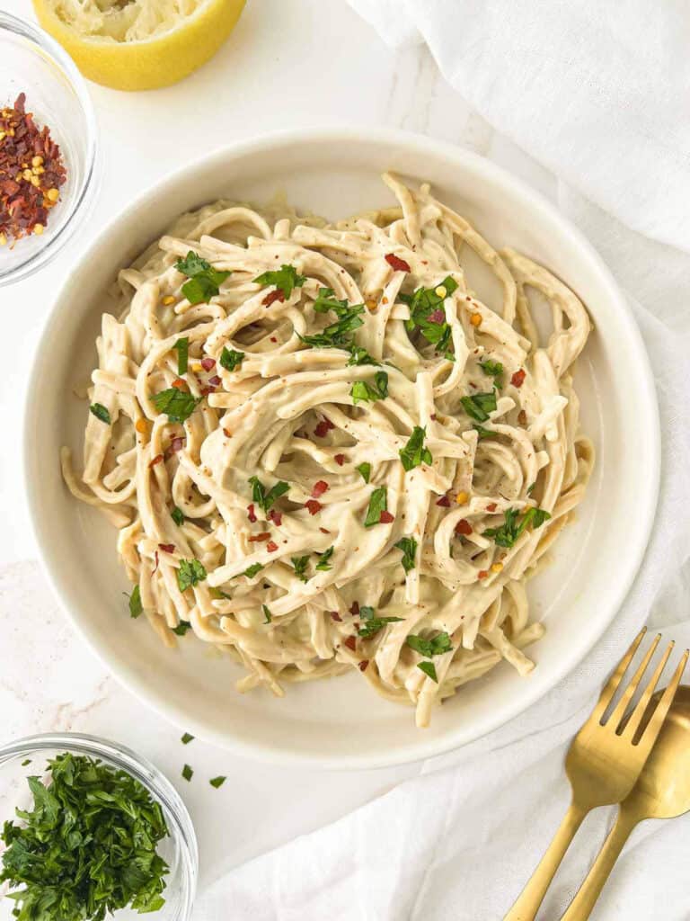 Creamy silken tofu pasta sauce tossed with pasta in a white dish.