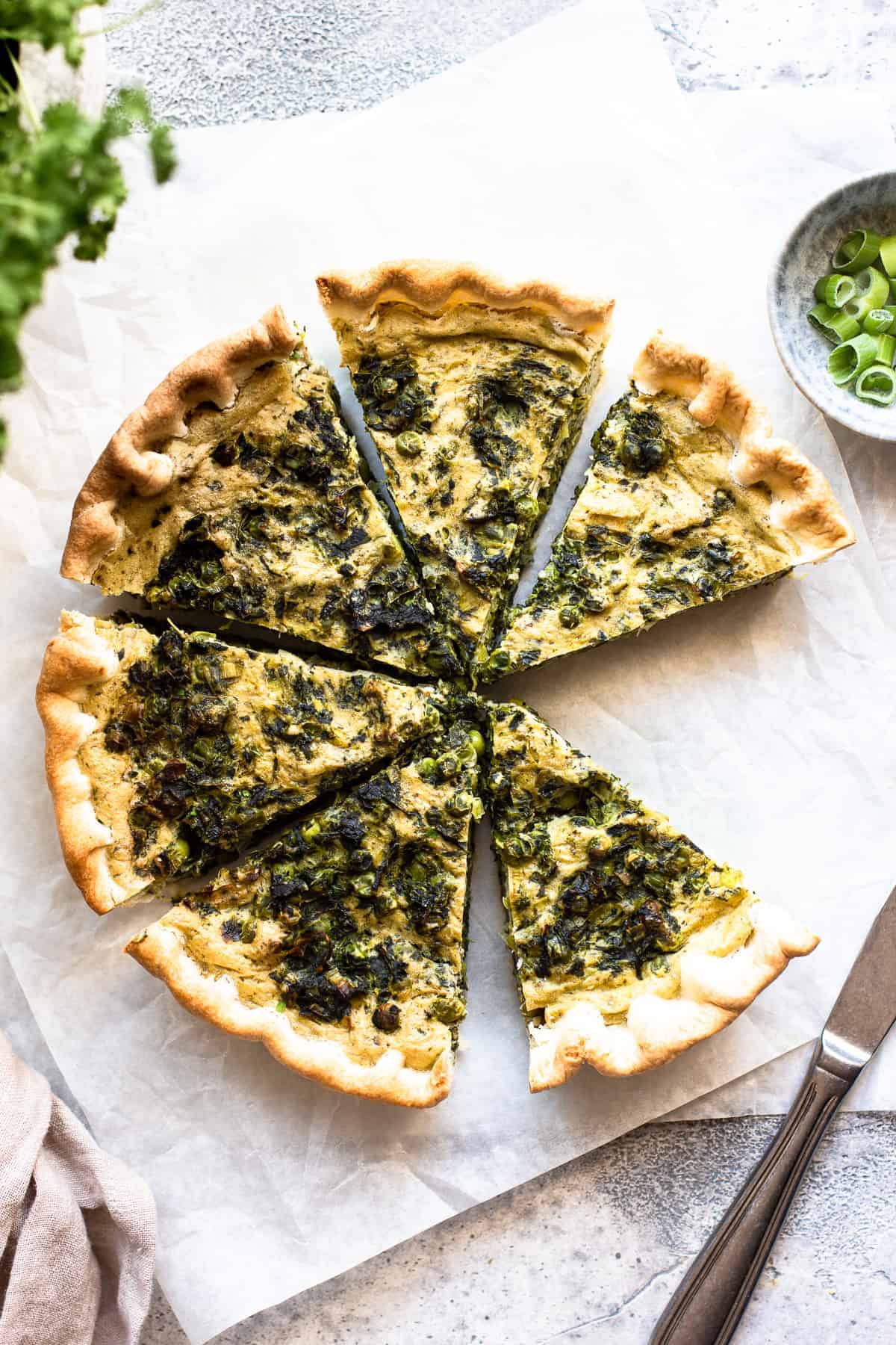 Vegan spinach quiche sliced with one piece missing.