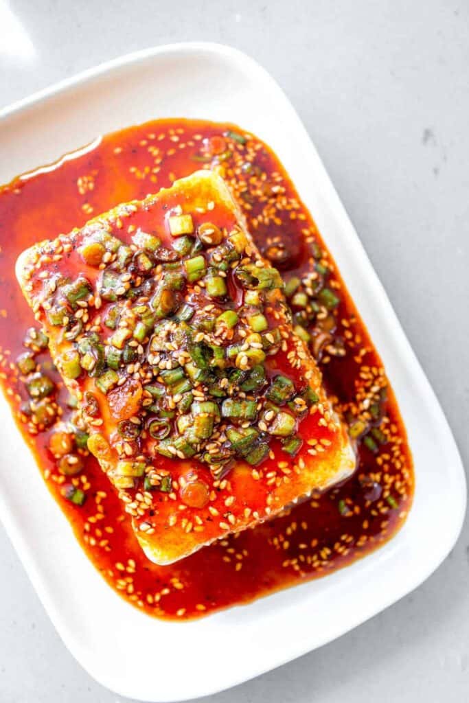 Silken tofu block smothered in a sesame soy sauce on a white dish.