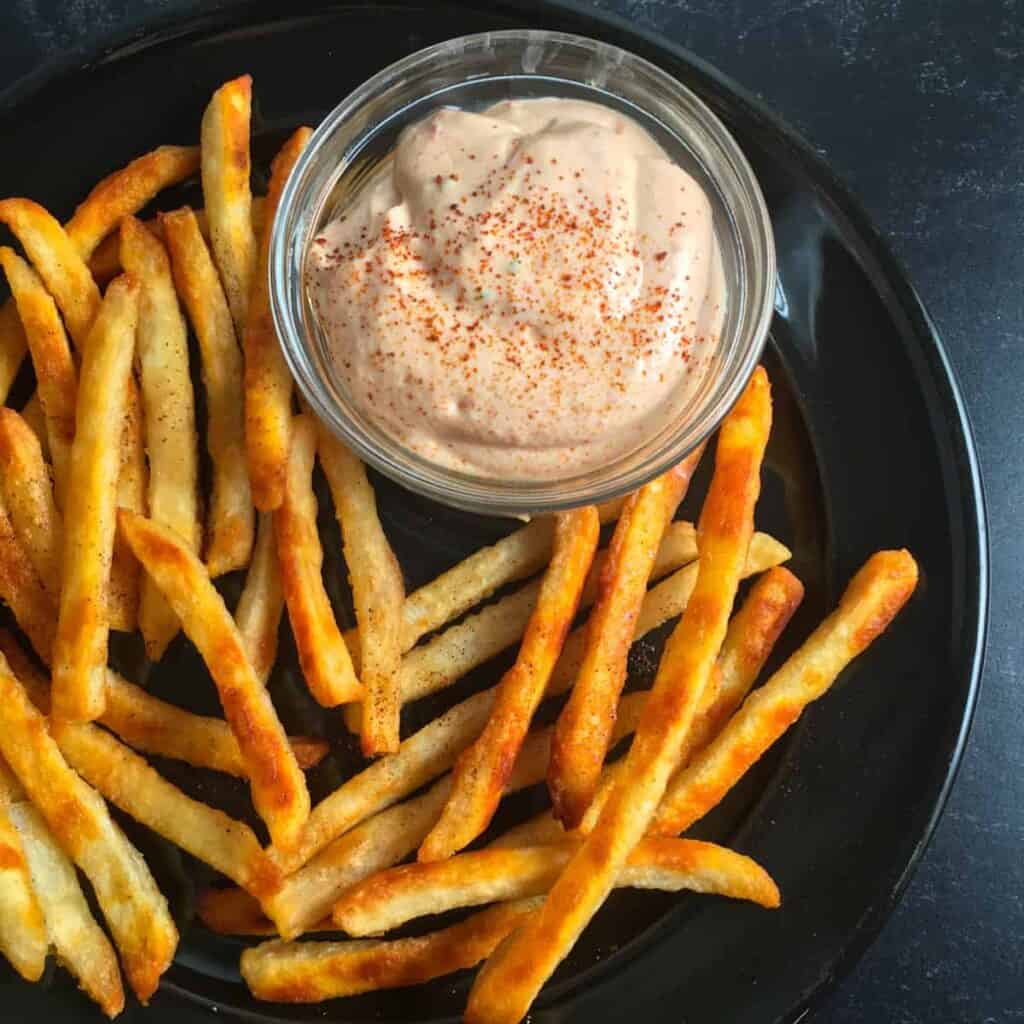 Chipotle mayonnaise in a glass bowl paired with fries on a black plate.