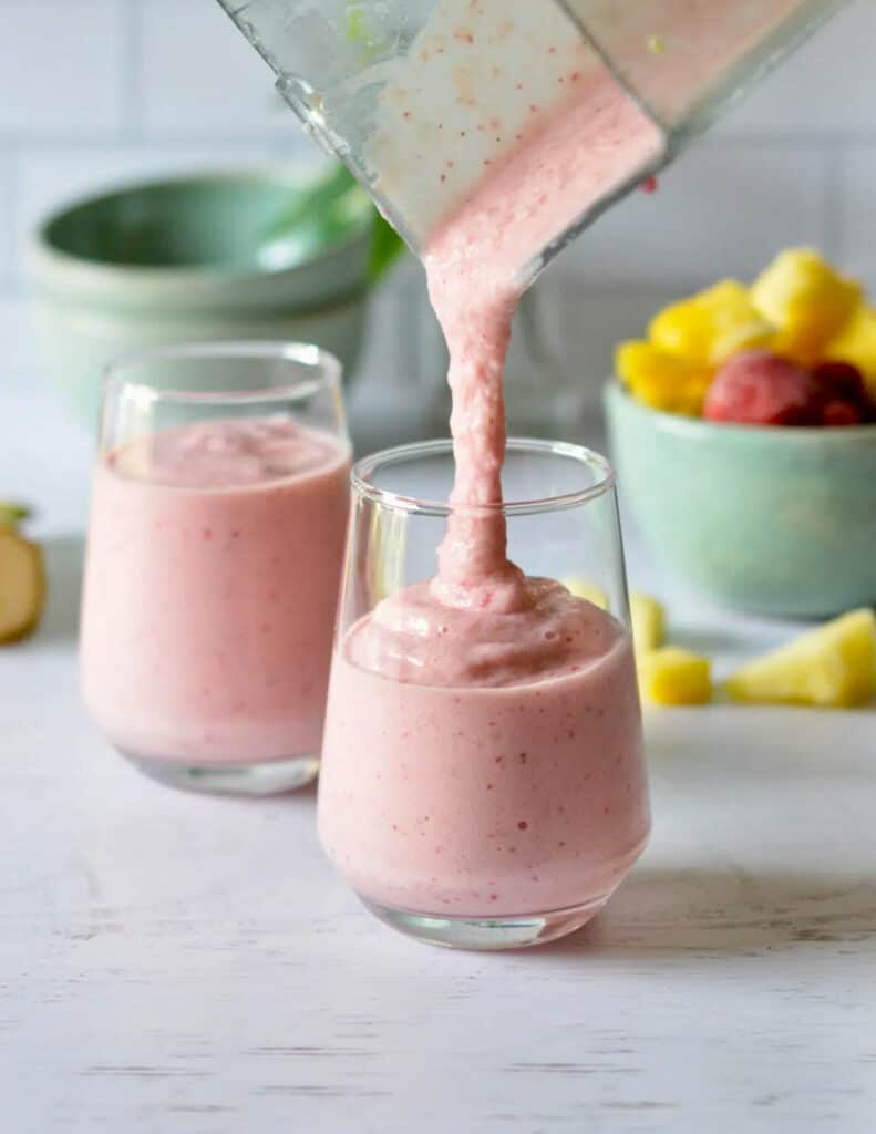 Pink strawberry smoothie being poured into a clear glass.