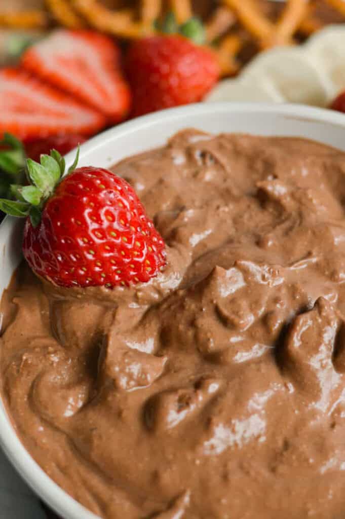 Close up of creamy chocolate dip in a white bowl with a whole strawberry garnish.