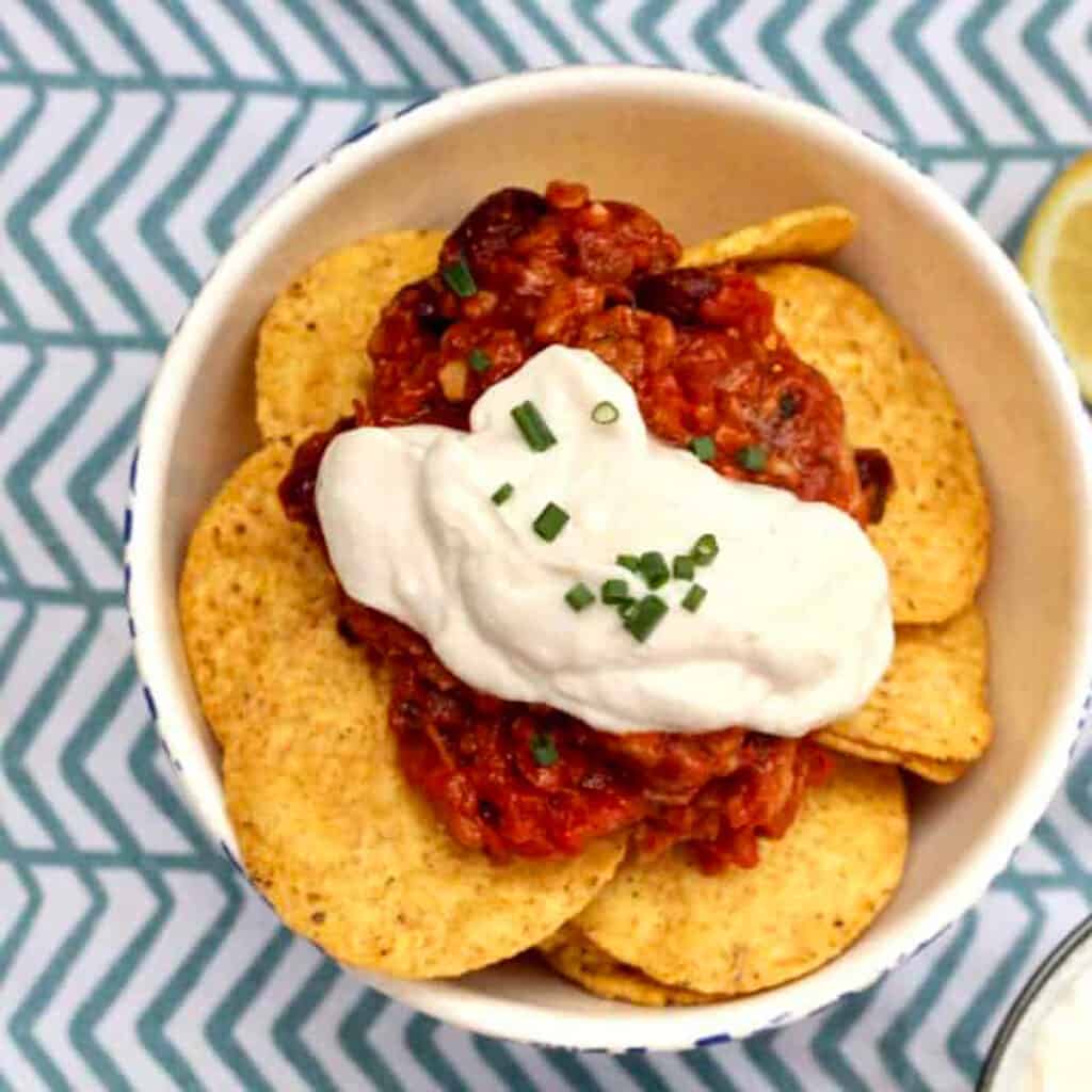 vegan sour cream dolloped on top of chips and salsa in a bowl.