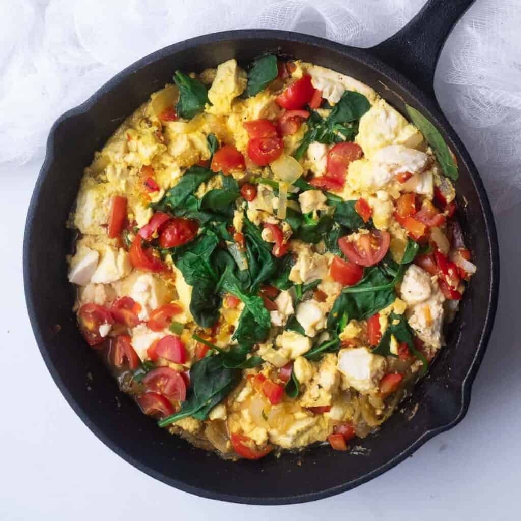 Tofu scramble with veggies in a black cast iron skillet.