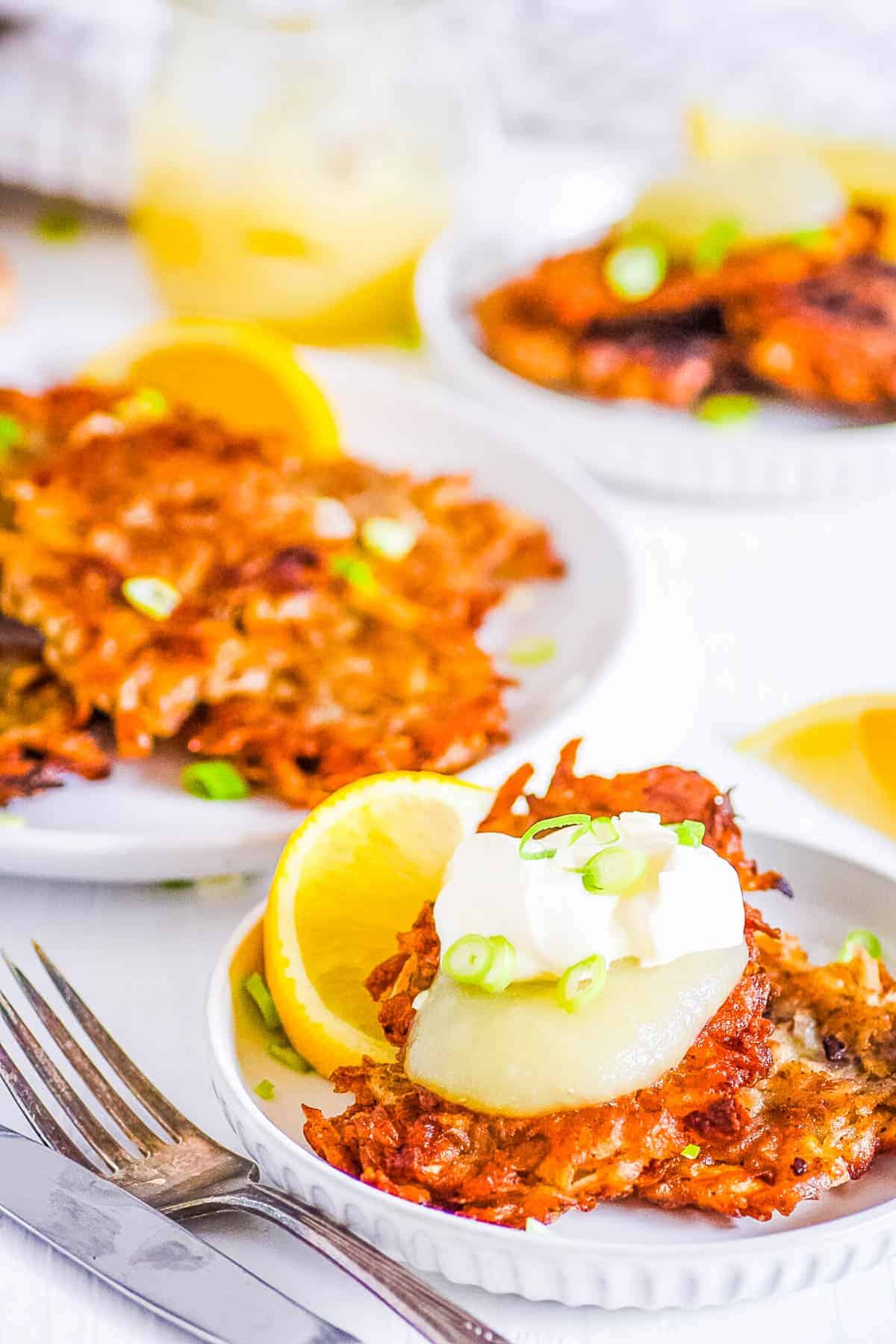 Potato pancakes topped with sour cream and green onions, with a lemon wedge, served on a white plate.