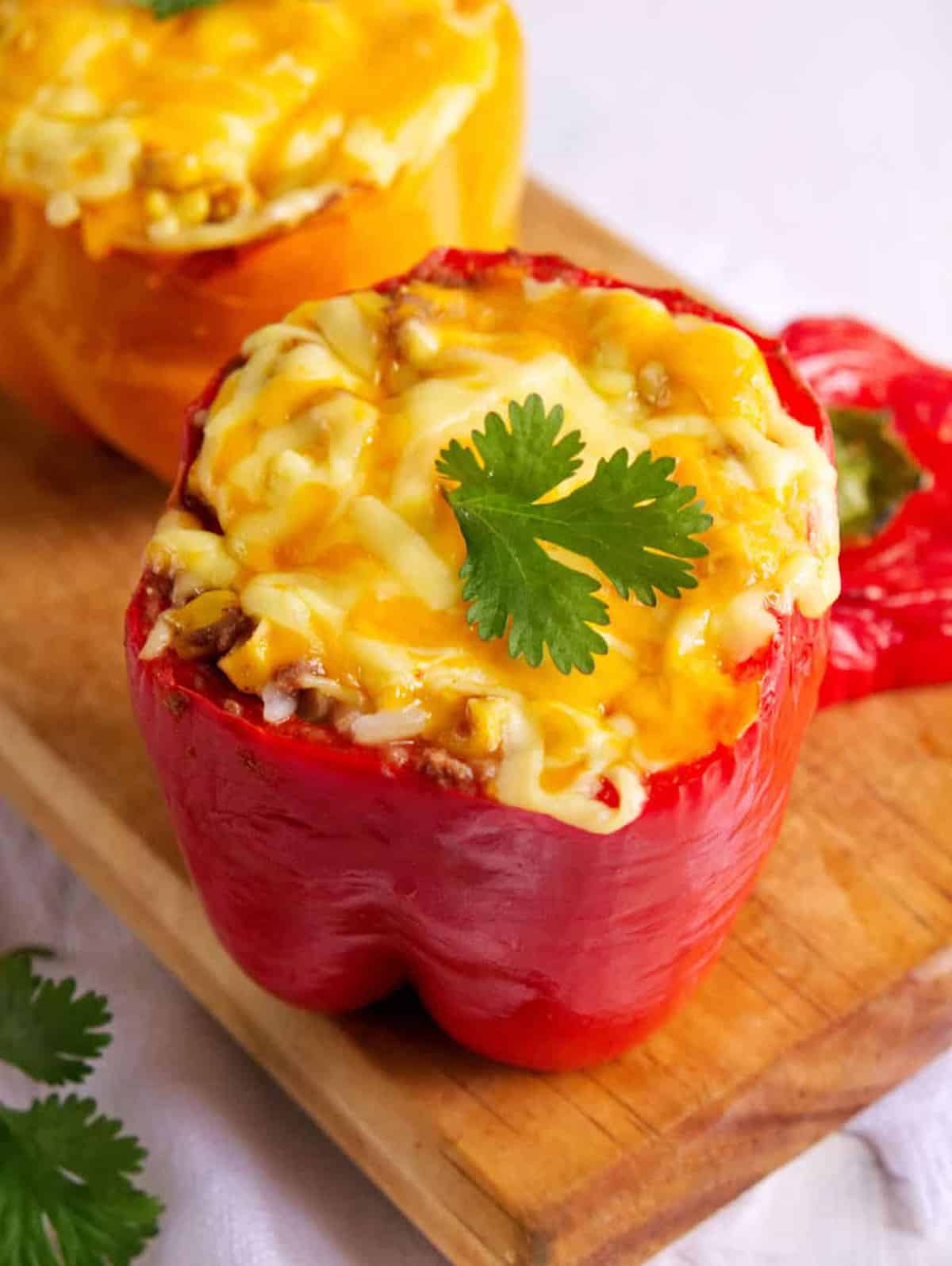 Stuffed bell pepper filled with veggies and melted cheese, on a wooden cutting board.