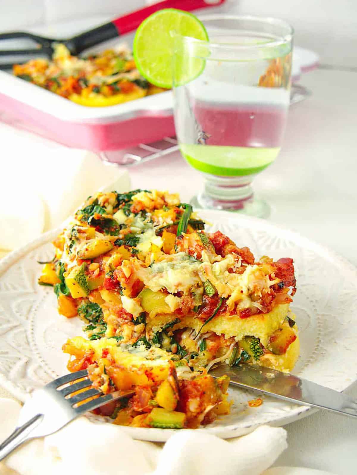 Polenta lasagna layered with melted cheese and vegetables on white plate.