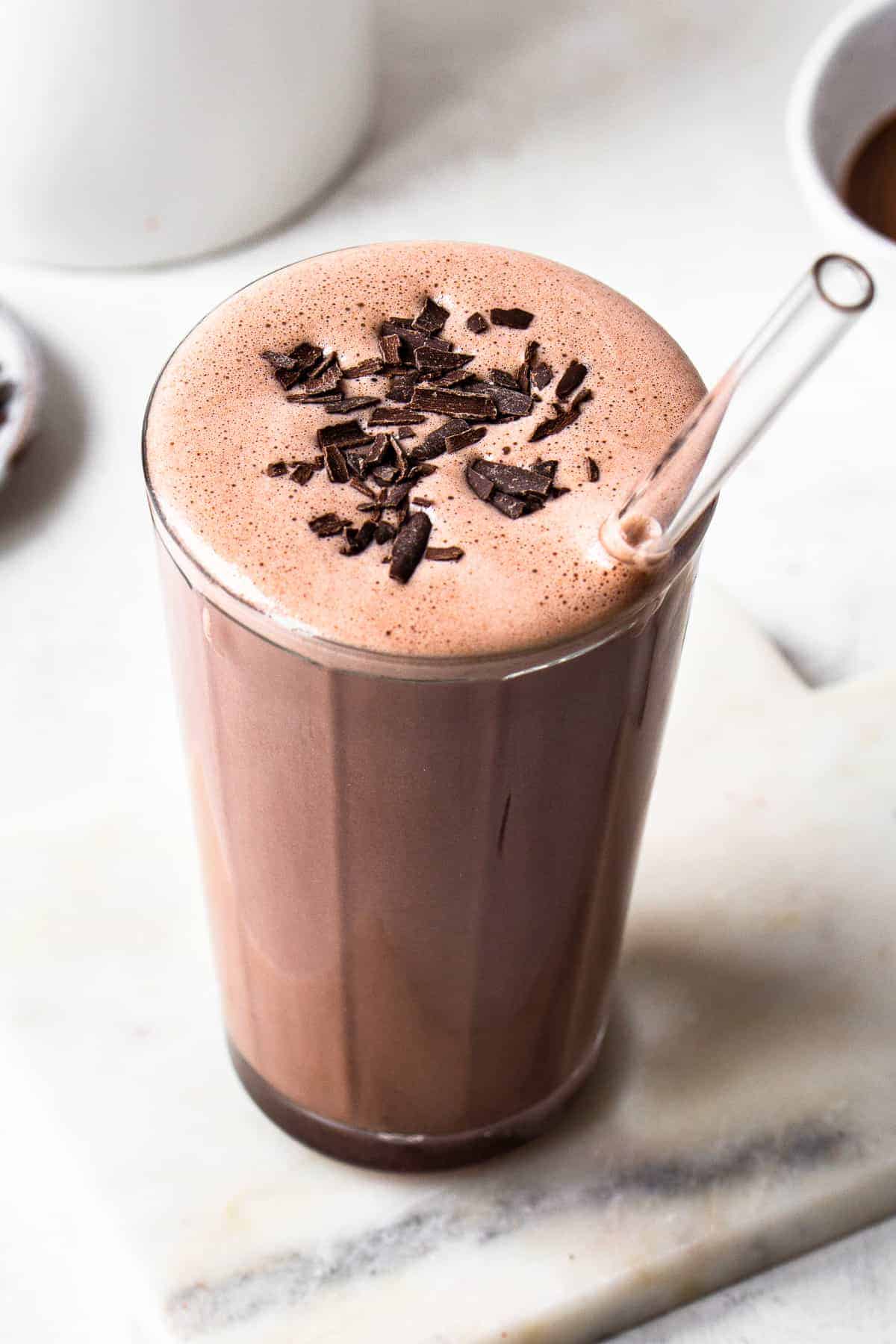 Chocolate silken tofu smoothie in a tall clear glass with chocolate shavings on top and a clear straw.