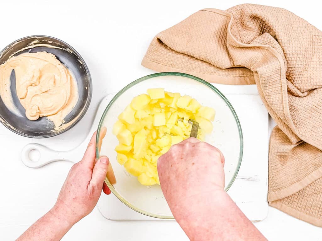 Potatoes being mashed in a mixing bowl.