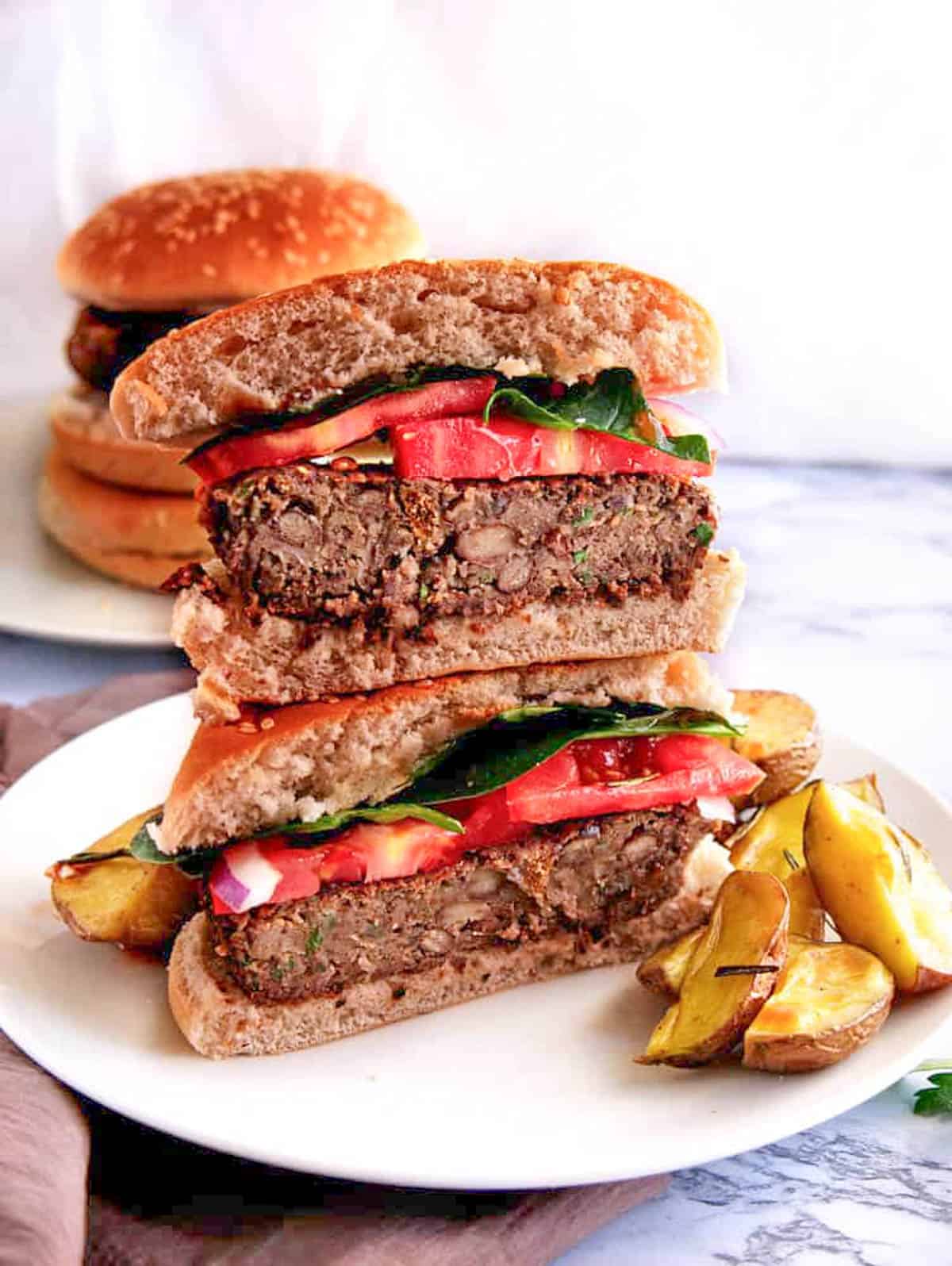 Black bean quinoa burgers cut in half, stacked on a white plate served with roasted potatoes on the side.