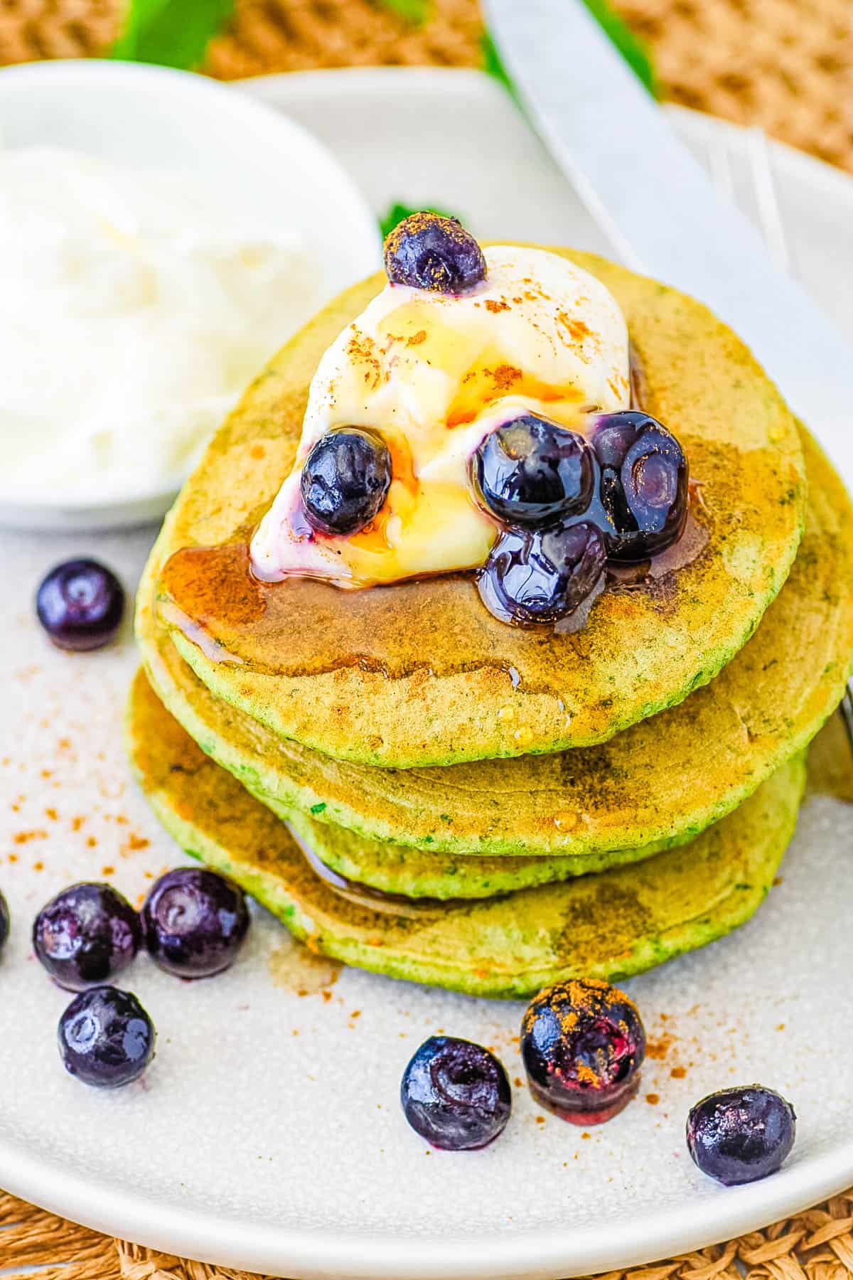 Easy spinach pancakes for kids, toddlers, or even adults stacked on a white plate, topped with berries and maple syrup.