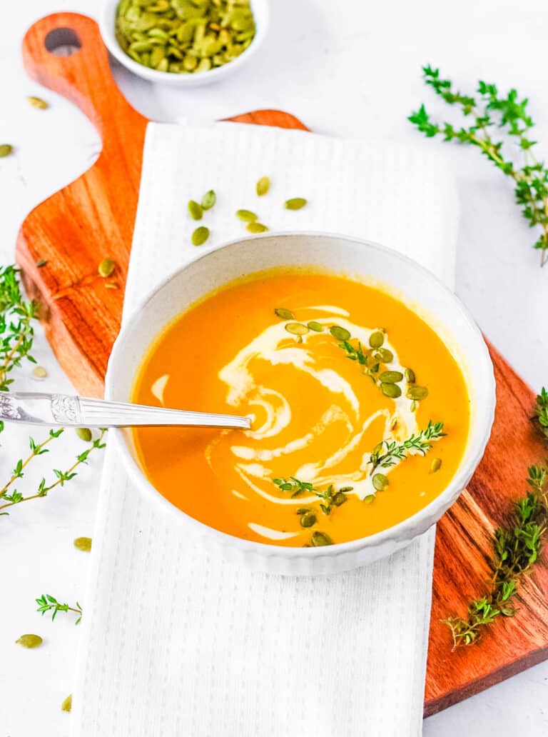 Butternut squash bisque, served in a white bowl, garnished with pumpkin seeds and a drizzle of cream.