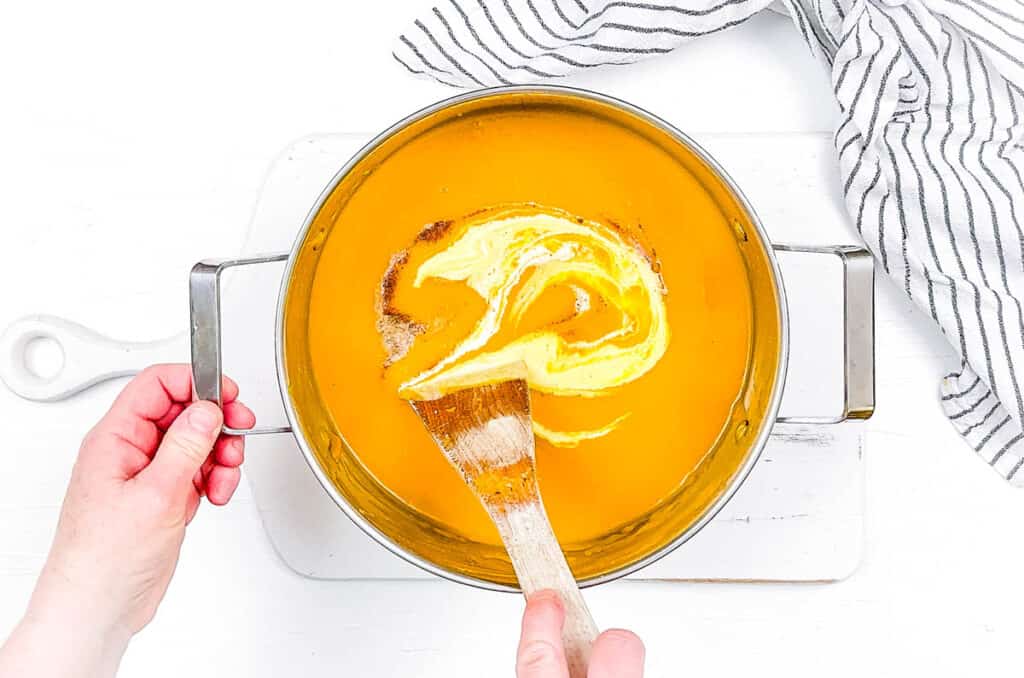 Butternut squash soup with heavy cream, cooking in a pot on the stove.