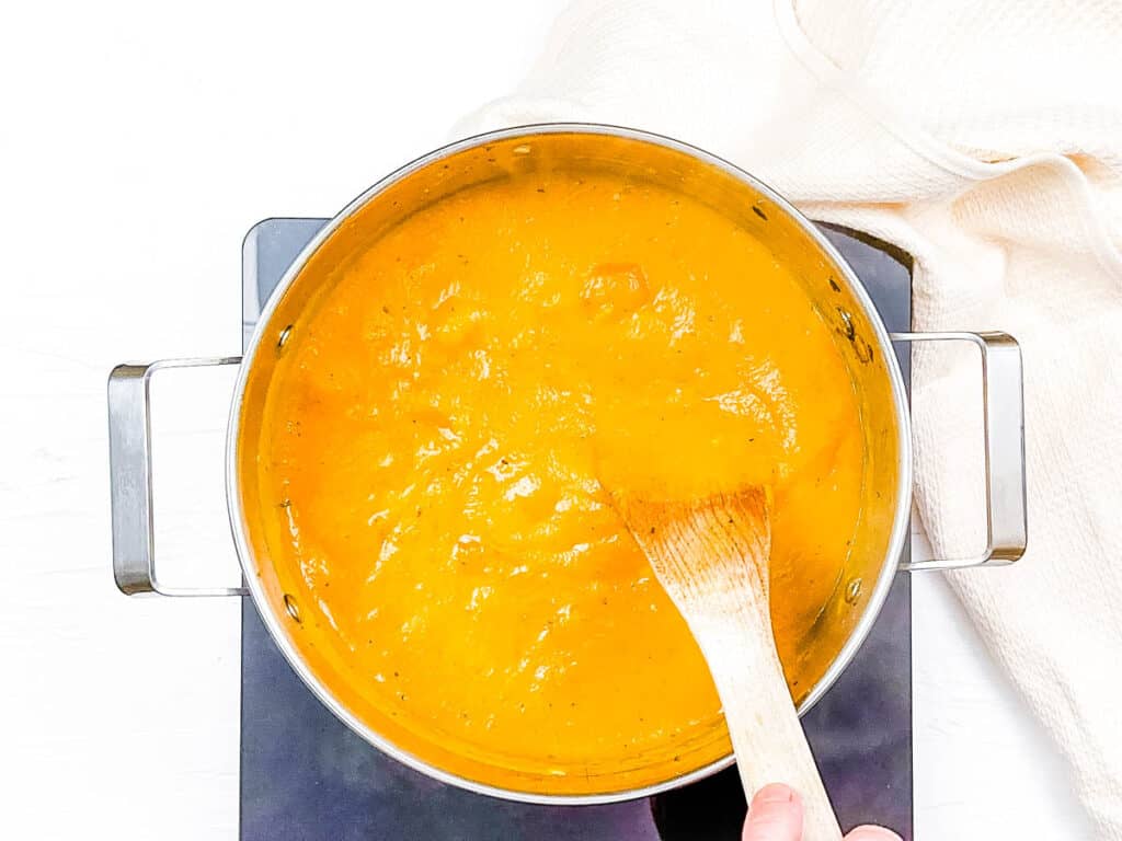 Carrot and potato soup cooking in a stock pot on the stove.