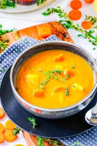 Carrot potato soup, served in a dark grey bowl, garnished with fresh herbs.