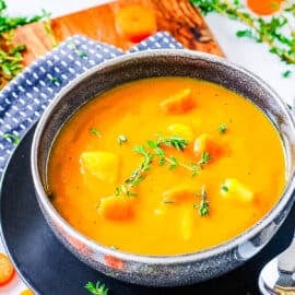 Carrot potato soup, served in a dark grey bowl, garnished with fresh herbs.