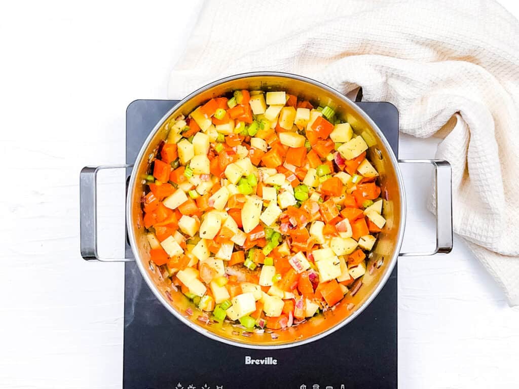 Potatoes, carrots, celery, onions, and spices cooking in a pot on the stove.