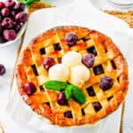 Cherry pie with frozen cherries on a white cutting board, topped with ice cream and garnished with mint.