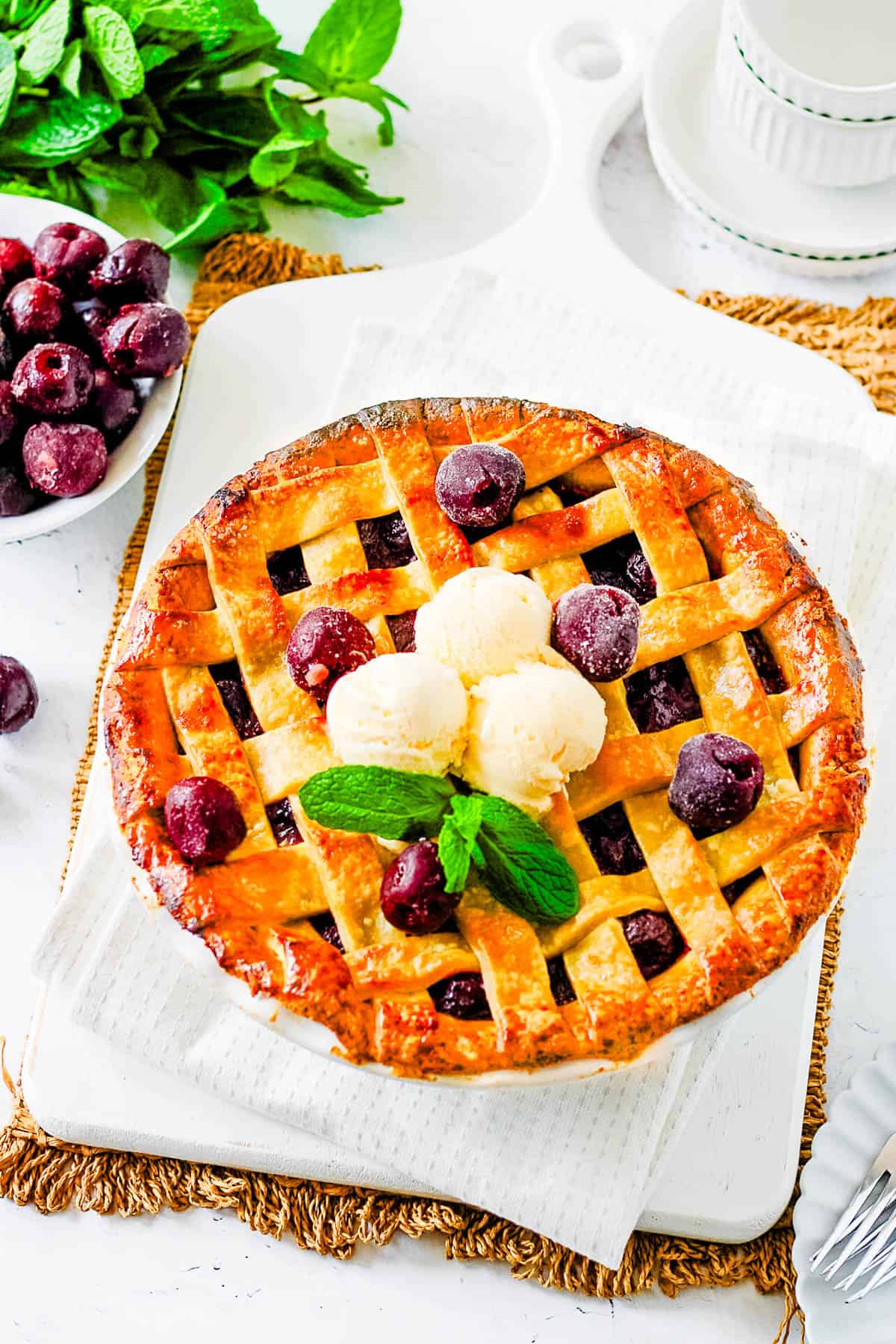 Cherry pie with frozen cherries on a white cutting board, topped with ice cream and garnished with mint.