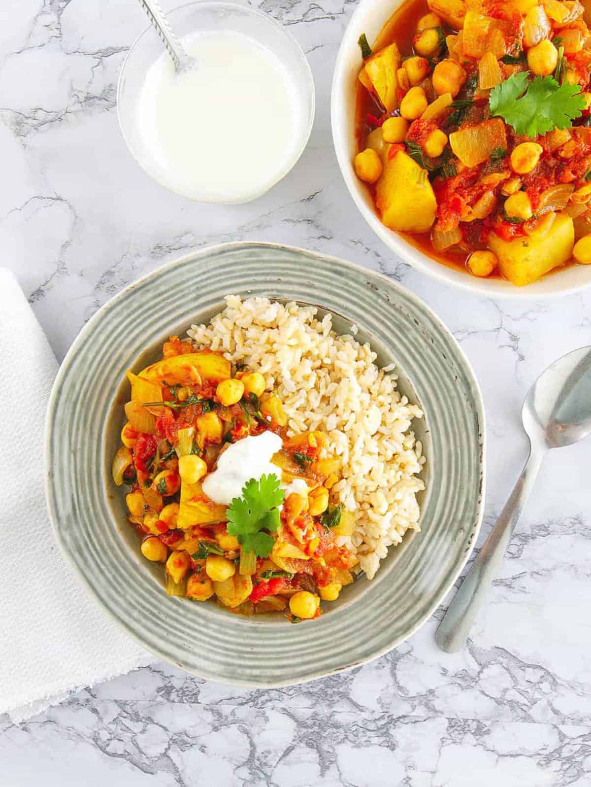 Vegan chickpea and potato curry served in a grey bowl with rice and yogurt on the side.