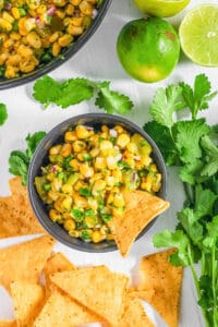 Easy Chipotle corn salsa served in a black bowl with a tortilla chip as a garnish.