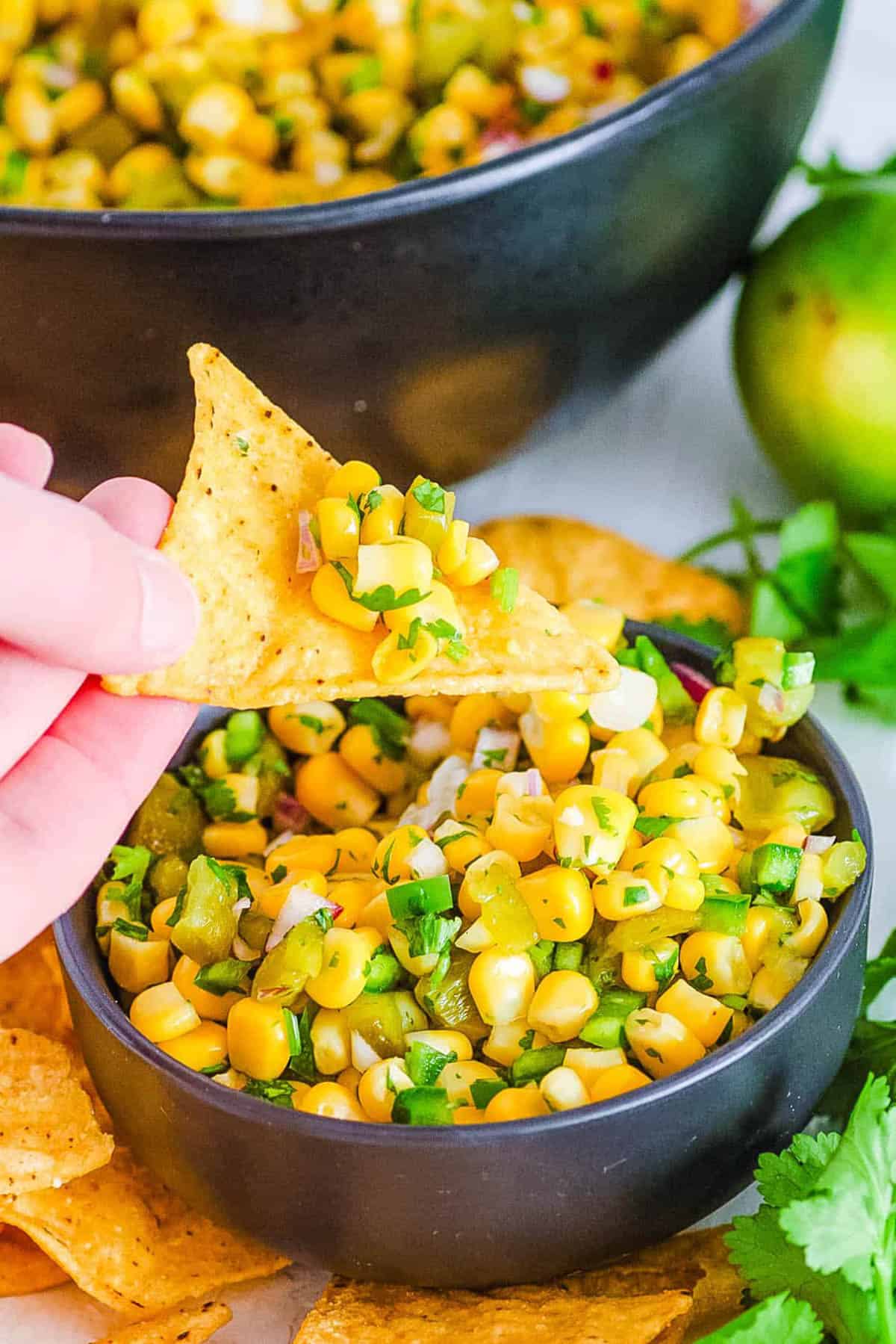 Chipotle corn salsa copycat recipe served in a black bowl with a tortilla chip as a garnish.