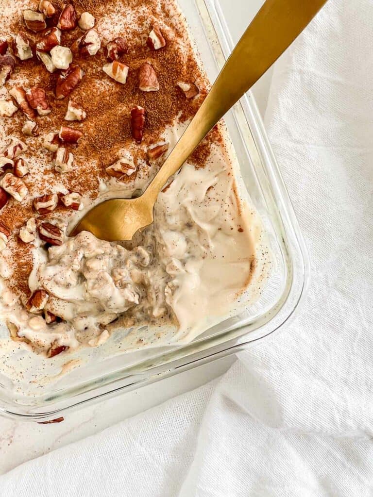 Cinnamon roll overnight oats in a glass serving dish topped with cinnamon and pecans.