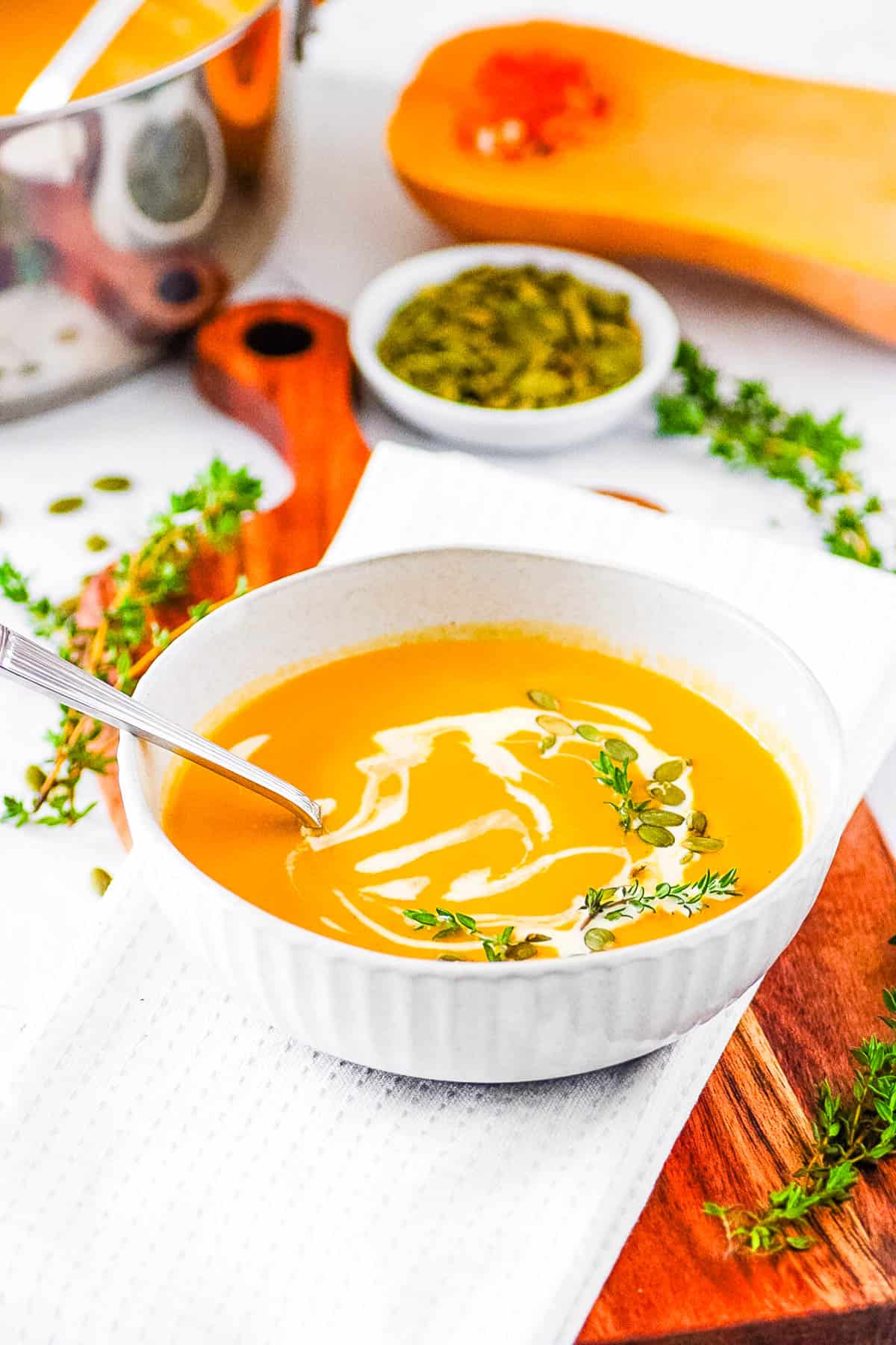 Butternut squash bisque, served in a white bowl, garnished with pumpkin seeds and a drizzle of cream.