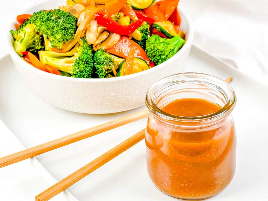 Low calorie stir fry sauce, served in a gl، jar with c،psticks and stir fried veggies on the side.
