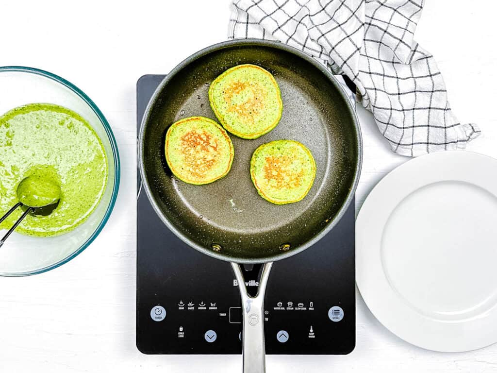 Green pancakes cooking in a pan on the stove.