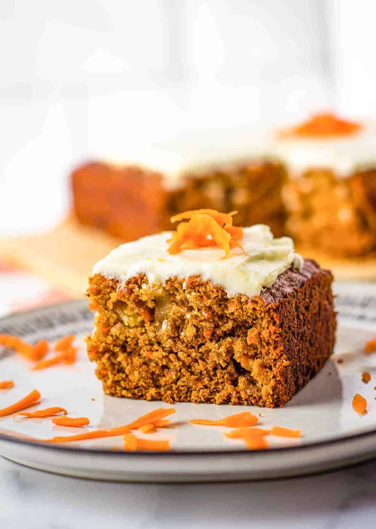 Slice of vegan carrot cake with vegan cream cheese frosting on a white plate.