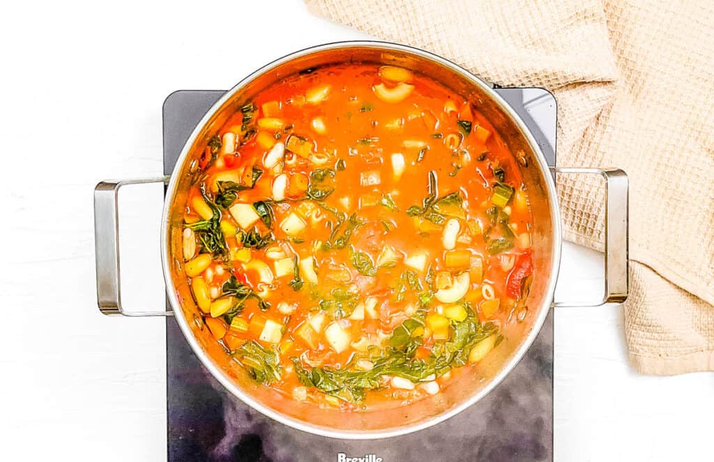 Plant based minestrone soup simmering in a large pot on the stove.