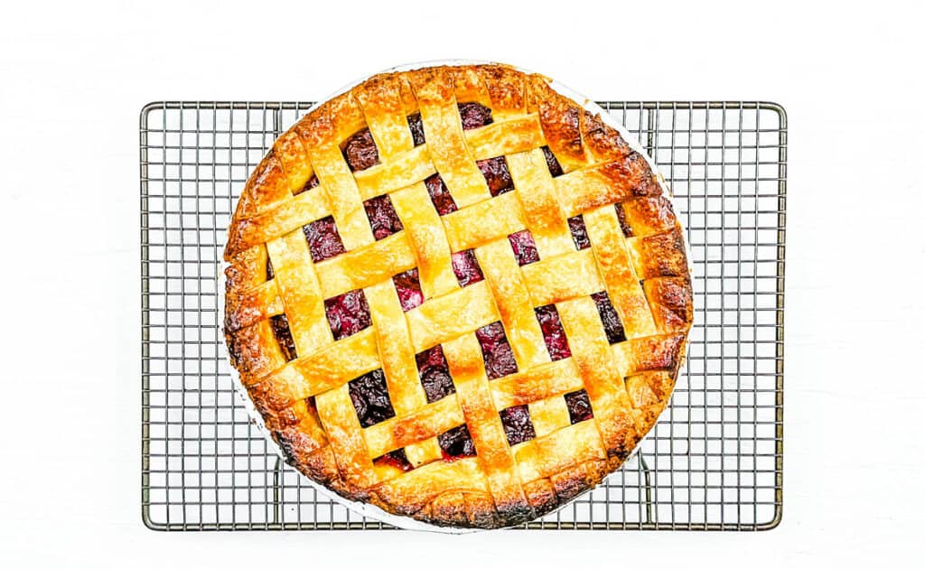 Homemade baked cherry pie with frozen cherries cooling on a wire rack.