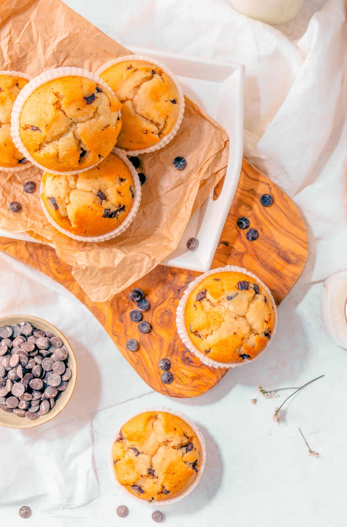 Gluten free banana chocolate chip muffins on parchment paper on a wooden cutting board.