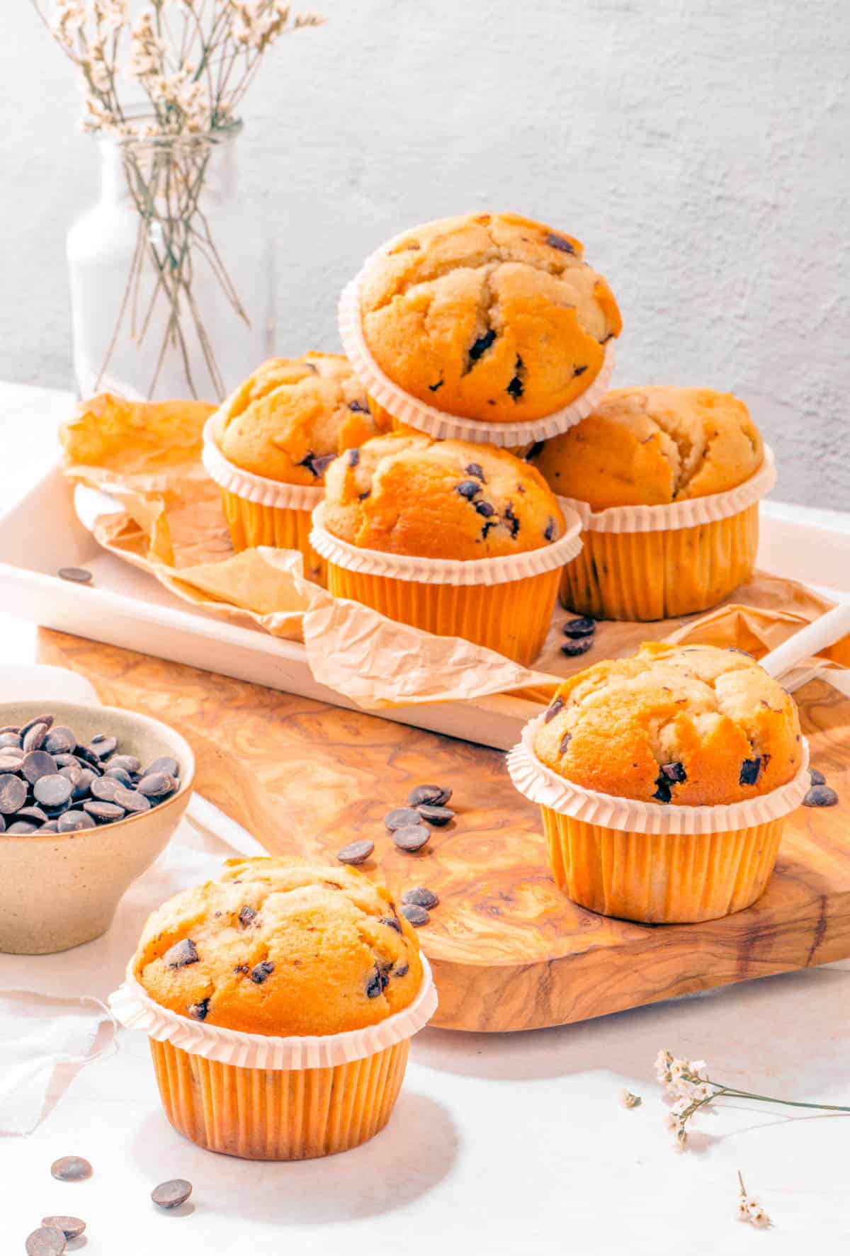 Gluten free banana chocolate chip muffins on parchment paper on a wooden cutting board.