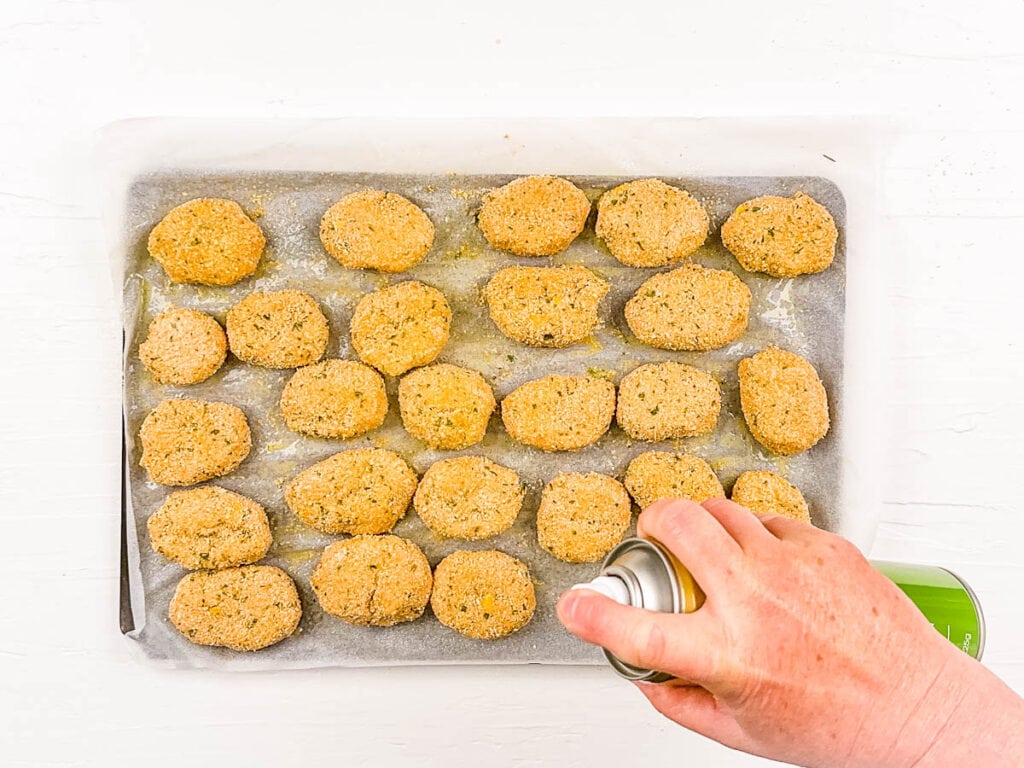Olive oil spray sprayed onto plant based nuggets on a baking sheet.