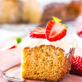 Slice of healthy gluten free tres leches cake topped with whipped cream and strawberries, served on a white plate.