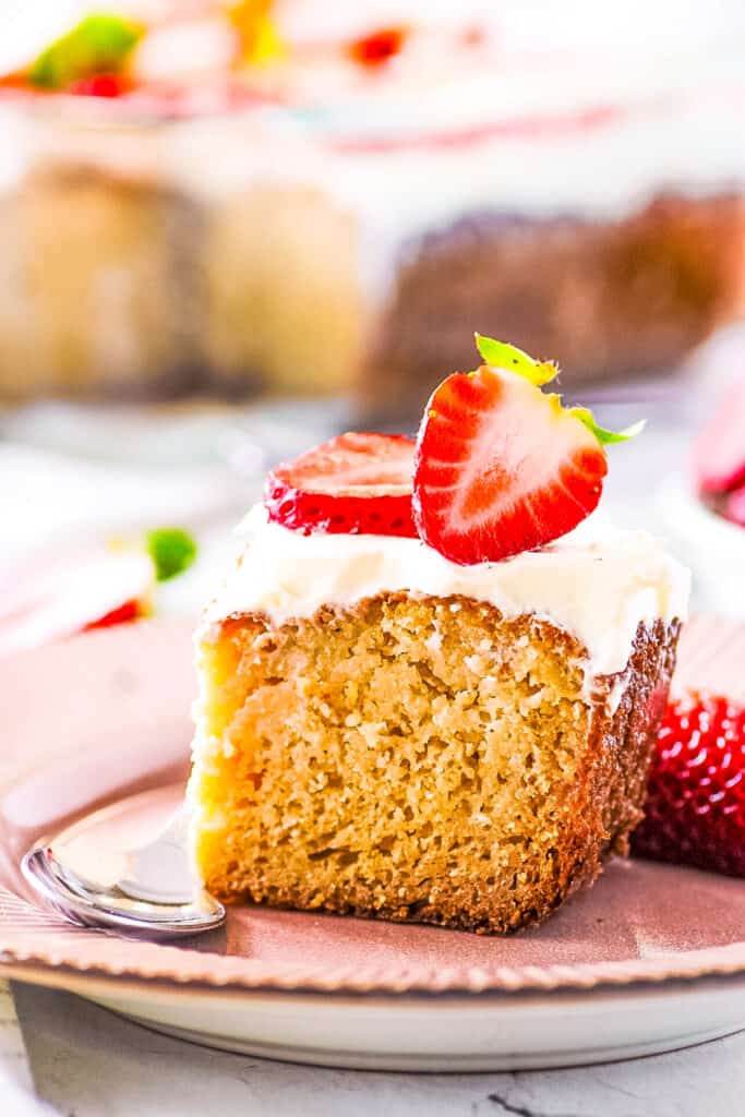 Slice of healthy gluten free tres leches cake topped with whipped cream and strawberries, served on a white plate.