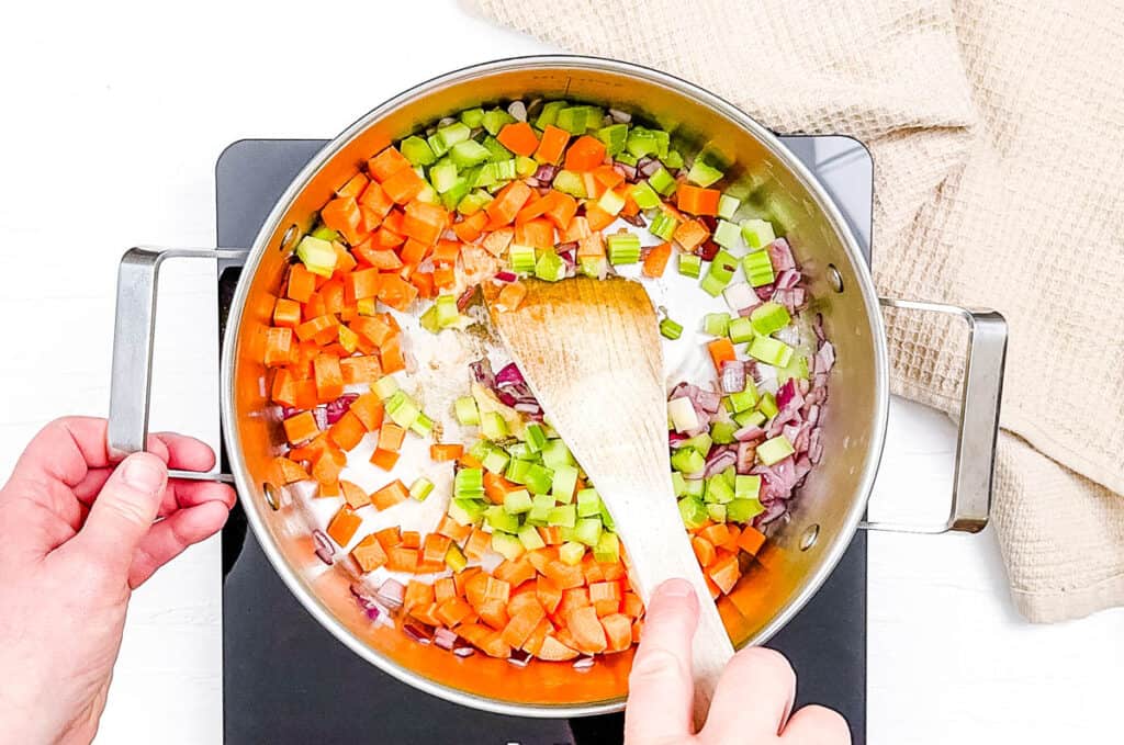 Onions, celery and carrots sauteeing in a large pot on the stove.