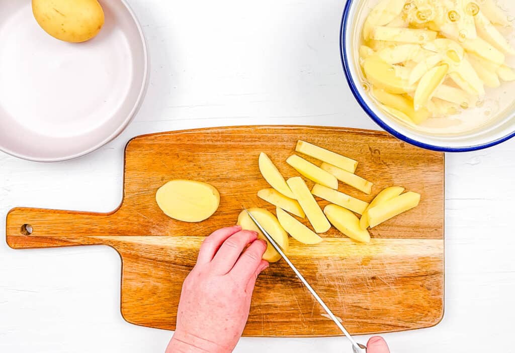 Potatoes being sliced into wedges on a cutting board.