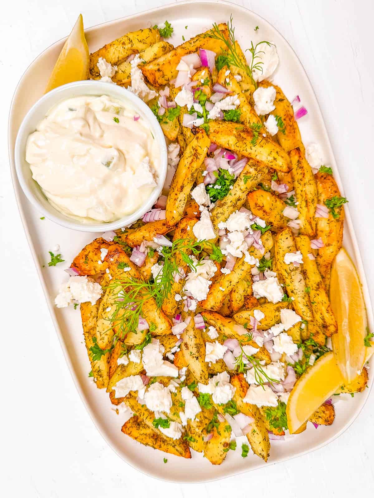 Loaded Greek french fries on a white plate, with tzatziki sauce on the side.