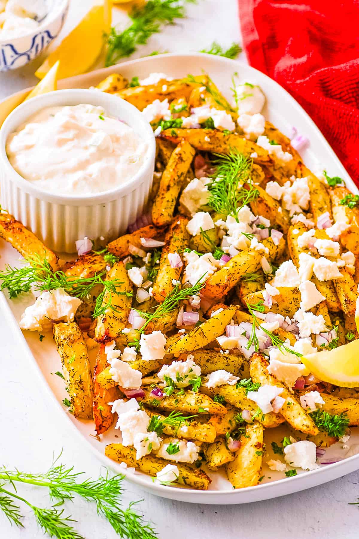 Easy Greek fries with feta, parsley, onions, and tzatziki dip on the side, served on a white plate.