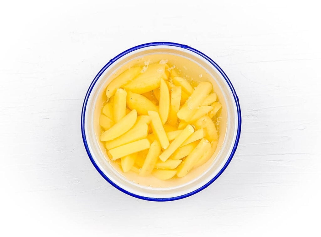 Potato wedges being soaked in water in a mixing bowl.