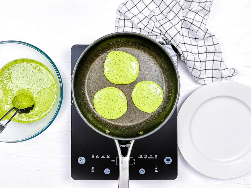 Grinch pancakes cooking in a skillet on the stove.