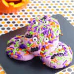 Purple Halloween monster cookies with googley eyes stacked on a black cutting board.