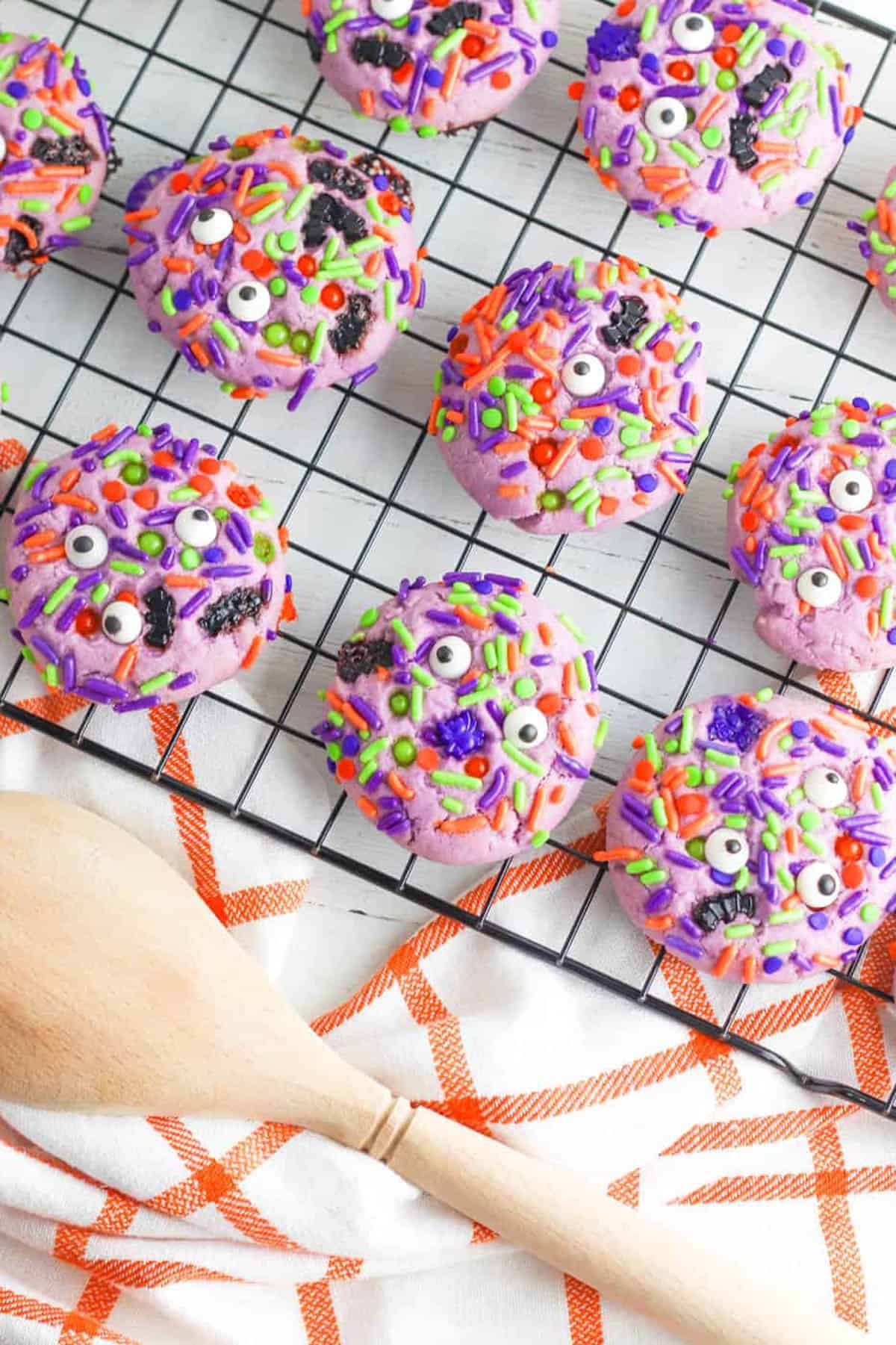 Purple Halloween monster cookies with googley eyes cooling on a wire rack.