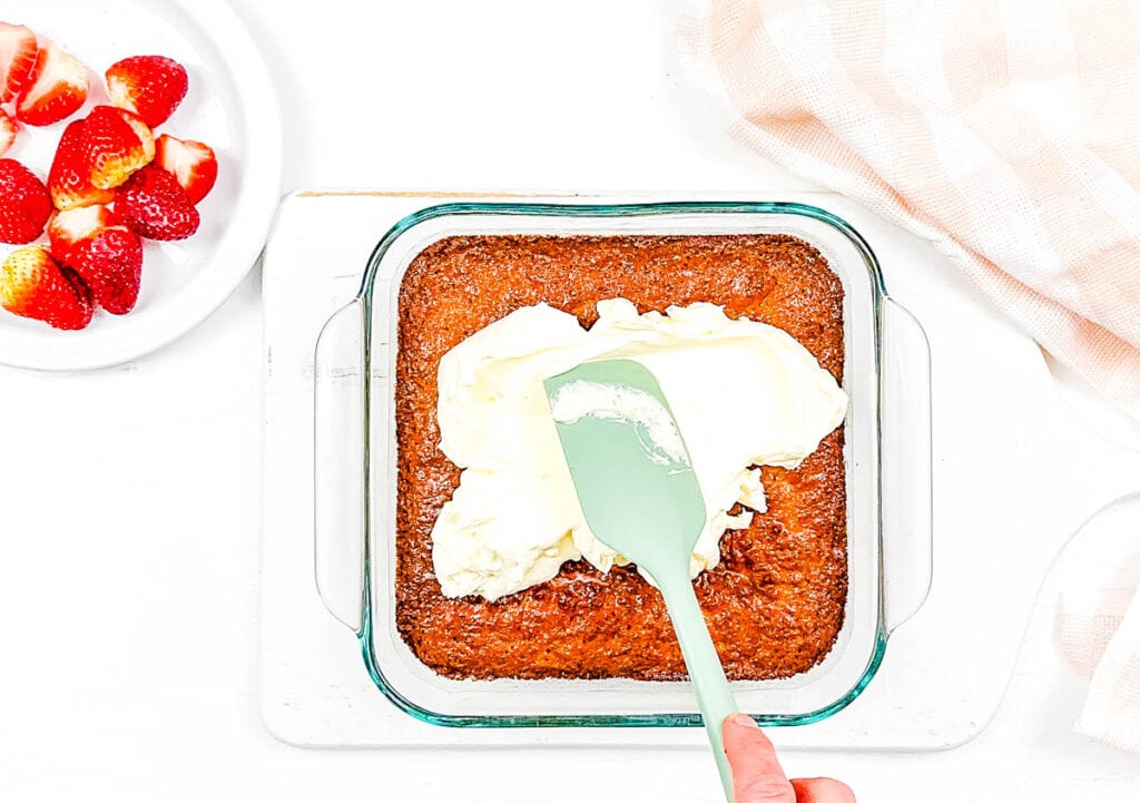 Whipped cream topping added to gluten free three milk cake in a baking dish.
