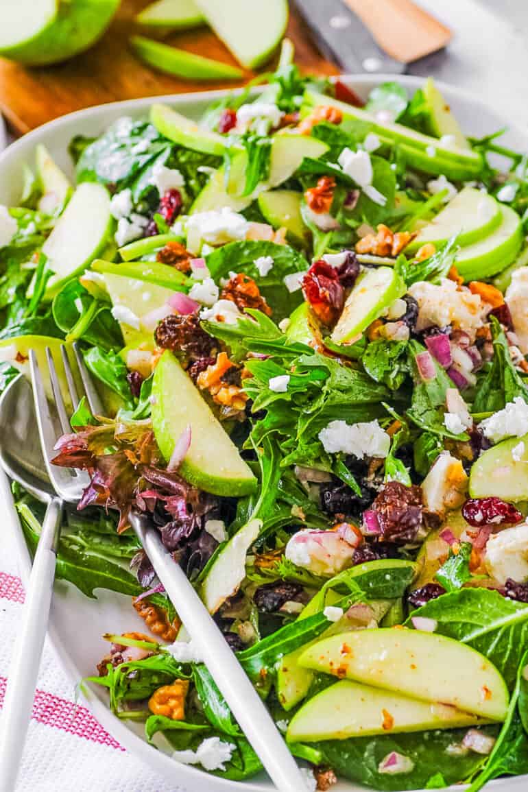 Apple walnut salad with cranberries, dates, and feta served on a white serving plate.