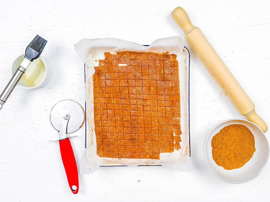Cinnamon sugar cereal being cut into squares on a baking sheet.