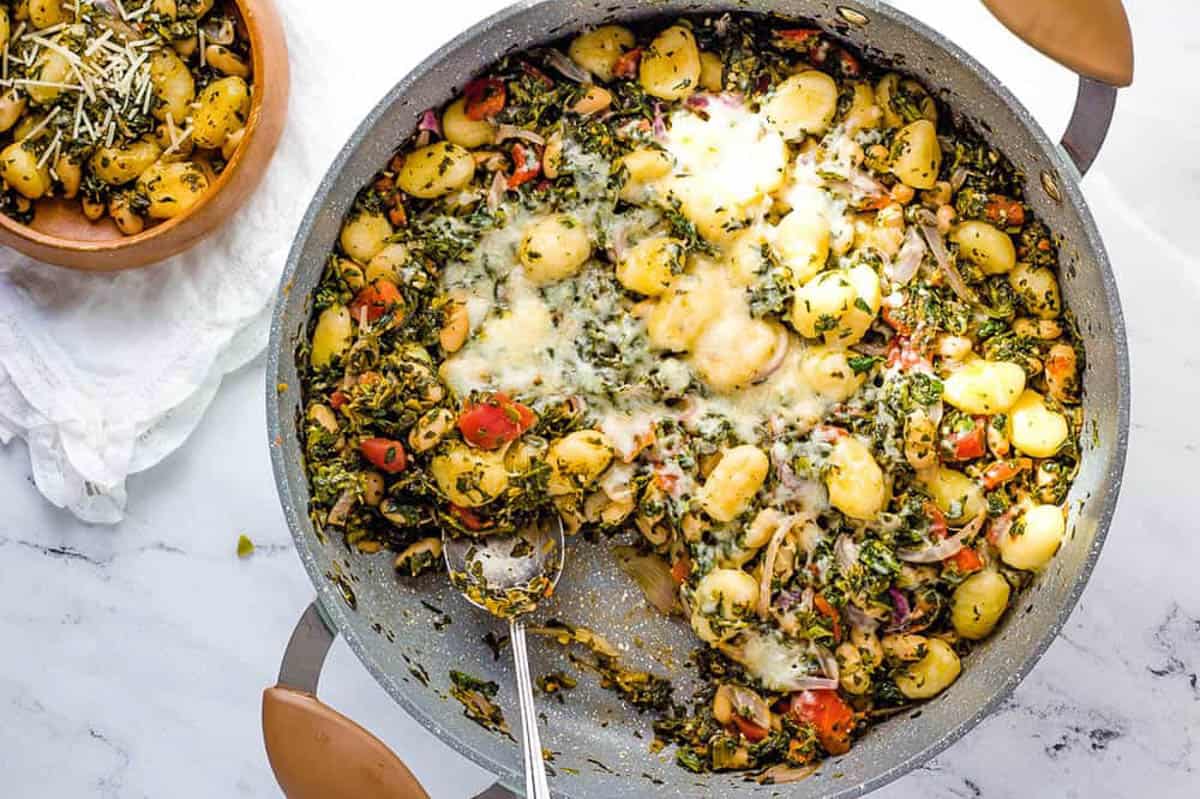 Healthy veggie gnocchi covered with mozzarella cheese served in a large skillet on the counter.